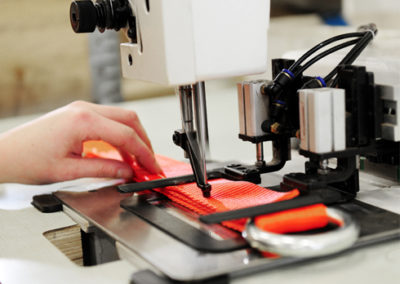Naai machine met hand die een oranje spanband naait